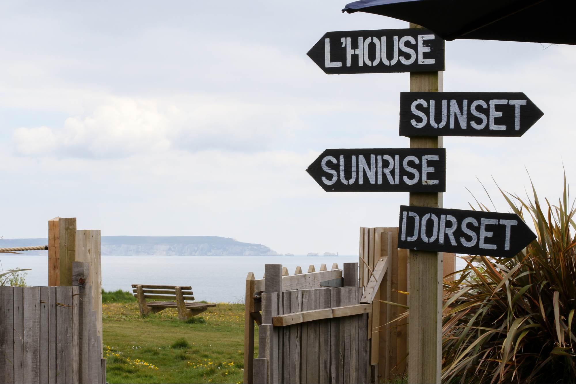 The signpost on the clifftop at Barton on Sea, pointing to the Lighthouse, Sunset, Sunrise and Dorset, with The Needles across the water