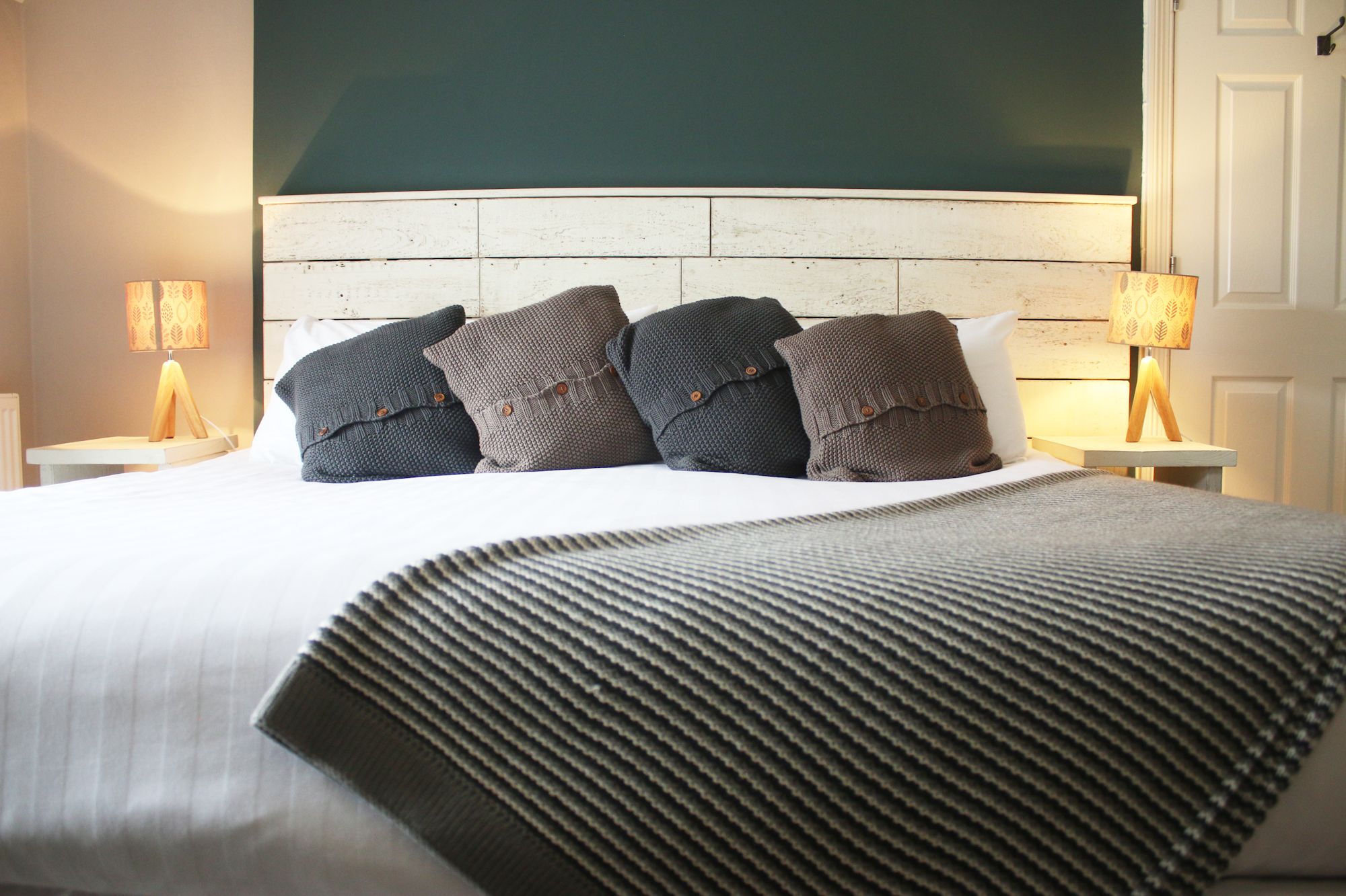 A bedroom at The Cliff House with a wooden headboard and soft grey throws